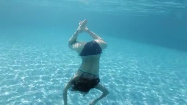 Una adolescente está nadando y jugando bajo el agua en la piscina en el agua clara. Soplando burbujas y mirando a la cámara . — Vídeos de Stock