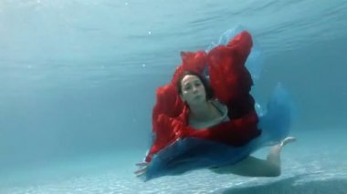 Elbiseli kıza havuzun alt kısmında kırmızı bir bez ile sualtı çalış ve kameraya benziyor.