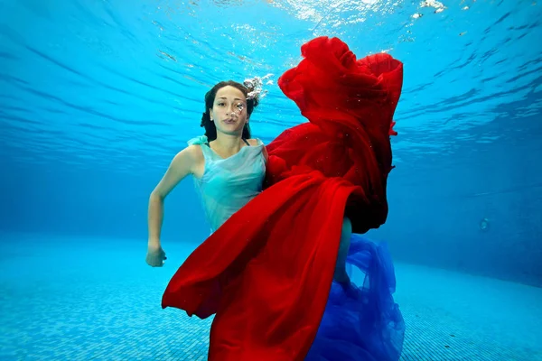 La chica juega bajo el agua con un paño rojo y mira a la cámara. Retrato. Disparos bajo el agua — Foto de Stock