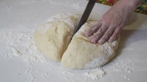 The girl cuts with a knife a large piece of dough into equal parts of a smaller size on a white table. — Stock Video