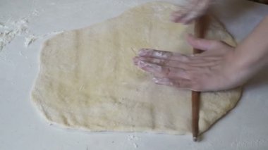 Kadın ahşap bir oklava ile beyaz bir tabloda hamur rulo.