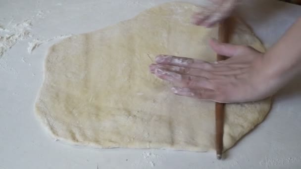 Женщина выкатывает тесто на белый стол деревянной скалкой . — стоковое видео