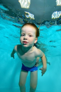 Küçük çocuk su altında bir kuş gibi yüzüyor ve kameraya benziyor. Portre. Yakın çekim. Su altında çekim. Aşağıdan manzara. Dikey yönlendirme