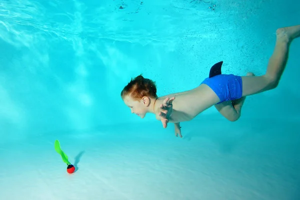 Menino feliz mergulha para um brinquedo debaixo da água na piscina e sorri. Retrato. Vista horizontal — Fotografia de Stock
