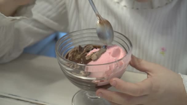 La petite fille mélange du chocolat et de la crème glacée aux fraises dans une tasse . — Video