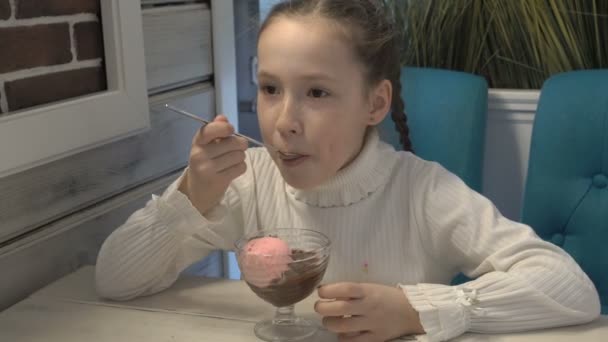 Ένα μικρό κορίτσι με φακίδες στο πρόσωπό της, κάθεται σε μια καφετέρια και τρώγοντας παγωτό. — Αρχείο Βίντεο