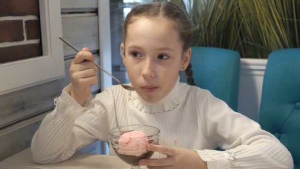 Une petite fille s'assoit dans un café et mange de la glace au chocolat. Gros plan, détail élevé . — Video