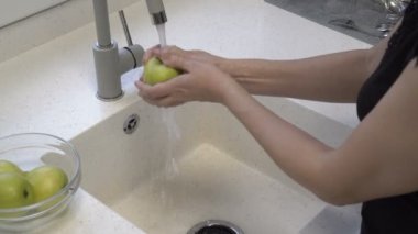An adult girl washes beautiful green apples under a stream of water in the kitchen sink and puts them on a black plate. Homework. Healthy diet. Closeup. 4k.