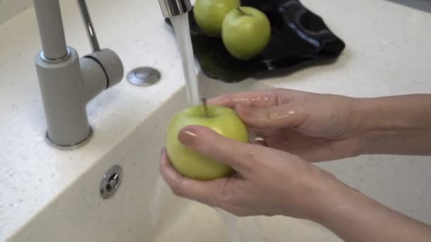 Gros plan, une femme lave soigneusement une belle pomme verte sous un ruisseau d'eau dans l'évier de la cuisine. Les devoirs. Une alimentation saine. 4k . — Video