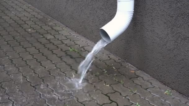 When it rains in the city, water pours from a white drainpipe onto the city sidewalk. Conceptualism. Symbol. Closeup. 4K. — Stock Video