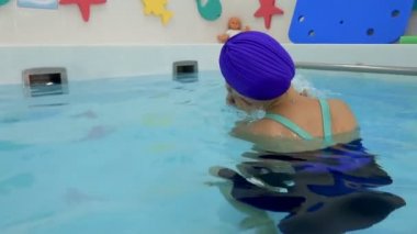 A happy mother is swimming with a newborn baby in the water in the children's pool. She supports the baby with her hands, hugs him and kisses him. Infant swimming in the children's pool. Closeup.