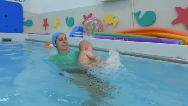 De moeder leert de baby zwemmen in het kinderbad. Het kind zwemt en schopt het water in. Zuigelingen zwemmen. Concept. Sluitingsdatum. — Stockvideo