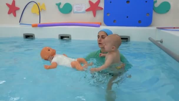 A crying baby swims with a swimming coach in a children's pool. Swimming training. Infant swimming. Closeup. — ストック動画