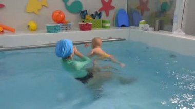 A female instructor is engaged in swimming with a baby in a children's pool. Swimming training. Infant swimming. Closeup.