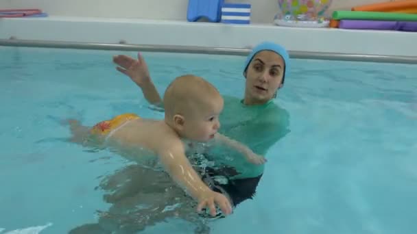 Een huilend jongetje zwemt in het water, in de armen van zijn moeder, in het kinderbad. De coach leert het kind zwemmen en ondersteunt hem. Zuigelingen zwemmen. Concept. Close-up. — Stockvideo