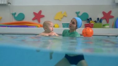 A happy baby and his adult mother are swimming and playing in the water in the children's pool. Infant swimming. Split shot. Underwater and on the surface. Closeup. Concept.