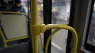 View from the interior of a bus traveling through the city. A close-up of the yellow handrail, followed by a blurry view of the bus interior and glass doors. Abstraction. 4K.