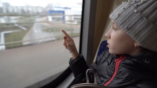 A little girl draws a heart on a fogged window in a traveling bus. View from inside the bus. Blurred background. Closeup. 4K. — Stok video