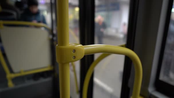 Uitzicht vanuit het interieur van een bus die door de stad rijdt. Een close-up van de gele leuning, gevolgd door een wazig zicht op het businterieur en glazen deuren. Abstractie. 4k. — Stockvideo