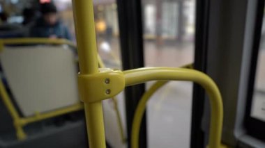 The bus pulls up to the stop, the glass doors open and a person enters the cabin. View from inside the bus. Faceless. Close-up of the yellow handrail. Blurred background. Abstraction. 4K.