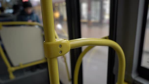 O ônibus pára até a parada, as portas de vidro se abrem e uma pessoa entra na cabine. Vista de dentro do autocarro. Sem rosto. Close-up do corrimão amarelo. Fundo desfocado. Abstração. 4K . — Vídeo de Stock