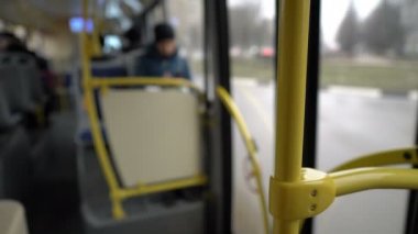 Şehirde seyahat eden boş bir otobüsün iç görüntüsü bulanık. İnsanlar, arabalar ve evler Windows 'un dışına taşınıyor. Sarı korkuluklara yakın çekim. Arka plan bulanık. Soyutlama. 4k.