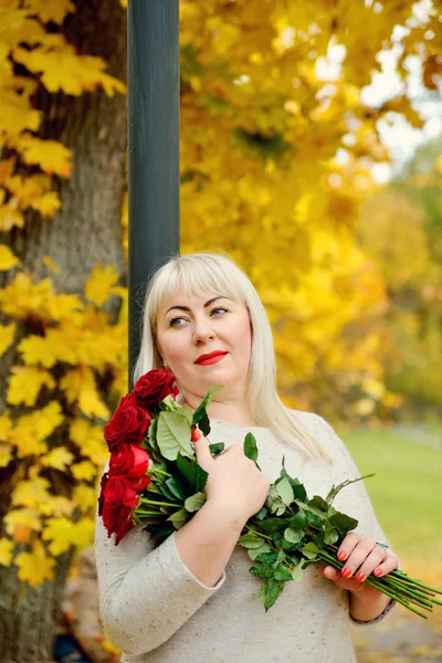 손에 붉은 장미를 들고 있는 꿈 속의 중년 크기의 여자가 노란 나뭇잎을 배경으로 밖으로 몸을 내밀고 있다. 클로즈업. 수직으로 본 모습. — 스톡 사진