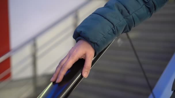 Una mujer golpea con el dedo la barandilla de una escalera mecánica de cristal que baja. Primer plano de la mano de una mujer en la barandilla de una escalera mecánica en movimiento en un centro comercial. Sin rostro. Concepto. 4K . — Vídeos de Stock