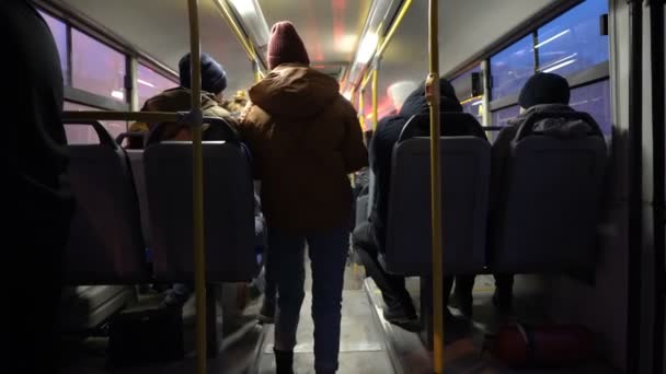 La gente camina y se mueve de un lugar a otro en el autobús que pasa por la ciudad nocturna. Las luces pasan por las ventanas. Vista desde la parte trasera del autobús. Fondo borroso. Concepto. 4K . — Vídeo de stock