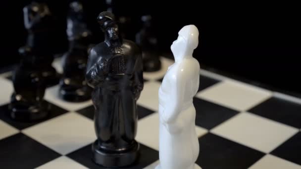Close-up, op een draaiend schaakbord zijn zwart-wit figuren in de vorm van Slavische volk-Kozakken. Wazige zwarte achtergrond. Concept. 4k. — Stockvideo