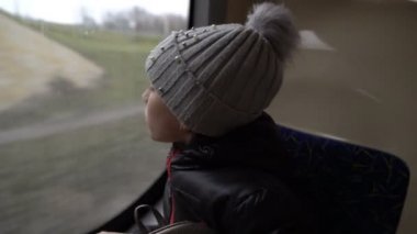 Küçük bir kız otobüs camında nefes alıyor ve tünelden geçen bir otobüsün arka koltuğunda otururken cama resim çiziyor. Otobüsün içinden bak. - Yakın çekim. Arka plan bulanık. 4k.