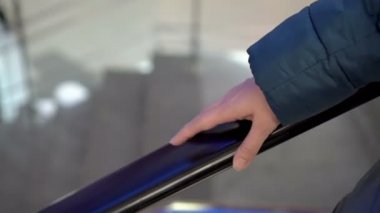 Bir kadın cam yürüyen merdivenden aşağı iniyor. Eli hareket eden bir yürüyen merdivenin korkuluğunda. Parmağını tırabzana vuruyor. - Yakın çekim. Yüzsüz. Kavram. 4K.