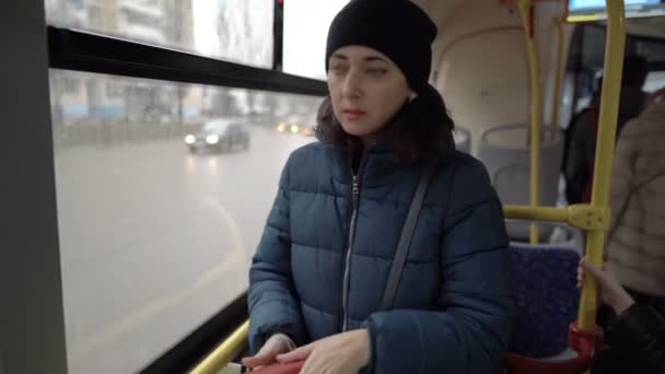 Smutna dorosła dziewczyna wyciąga kartę kredytową z portfela stojąc przy oknie w autobusie. Za oknem przejeżdżają samochody. Zbliżenie. Zamazane tło. 4k. — Wideo stockowe