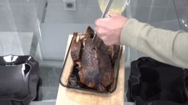 Adamın biri mutfaktaki ahşap bir kesme tahtasıyla büyük bir mutfak bıçağıyla ördek rosto kesiyor. Aile tatili. Yakın plan. Yüzsüz. 4k.