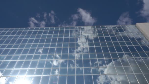 De ramen van het glazen gebouw van de wolkenkrabber reflecteren de blauwe lucht en wolken die op een zonnige dag door de lucht zweven. Concept. 4K. — Stockvideo