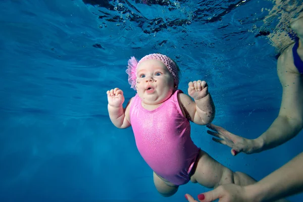 Sorprendido bebé bajo el agua en un traje de baño rojo sobre un fondo azul rodeado de burbujas. Una niña con ojos azules. Retrato de moda. Orientación horizontal — Foto de Stock