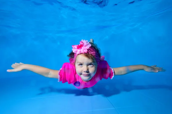 Una hermosa niña posa en el fondo de una piscina infantil con un vestido rojo, con los brazos extendidos sobre un fondo azul. Mira a la cámara y sonríe. Primer plano. Fotografía digital . — Foto de Stock