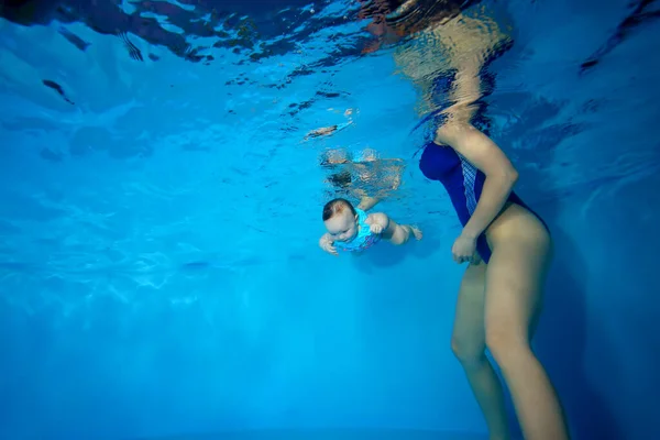 Uma mãe ensina um recém-nascido a nadar. Eles estão nadando em uma piscina infantil em um fundo azul. Foto digital. Orientação horizontal . — Fotografia de Stock