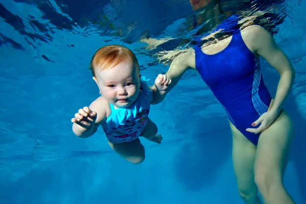 Close-up, una pequeña chica de ojos azules se sumerge en una piscina para niños sobre un fondo azul, y su madre la ayuda. Foto digital. Orientación horizontal . — Foto de Stock