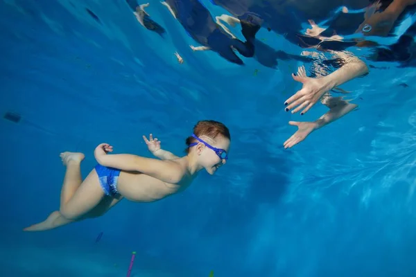 Un hermoso niño sonríe y nada bajo el agua en la piscina infantil para encontrarse con las manos de su madre. Concepto. De cerca. Foto digital. Vista horizontal . — Foto de Stock