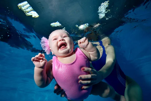 Primer plano de una niña llorando bajo el agua en una piscina infantil en un traje de baño rosa en los brazos de su madre. Concepto. Foto digital. Orientación horizontal . — Foto de Stock