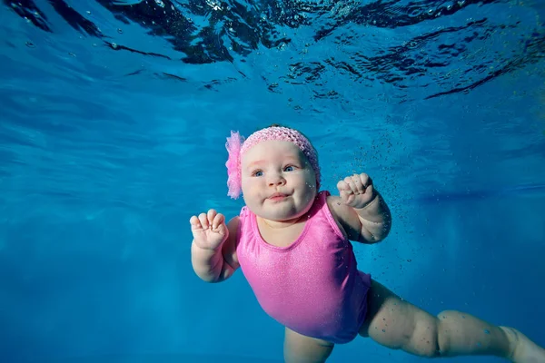 Retrato submarino de una encantadora niña nadando bajo el agua en una piscina infantil con un traje de baño rosa sobre un fondo azul. Concepto. Foto digital. Orientación horizontal . — Foto de Stock