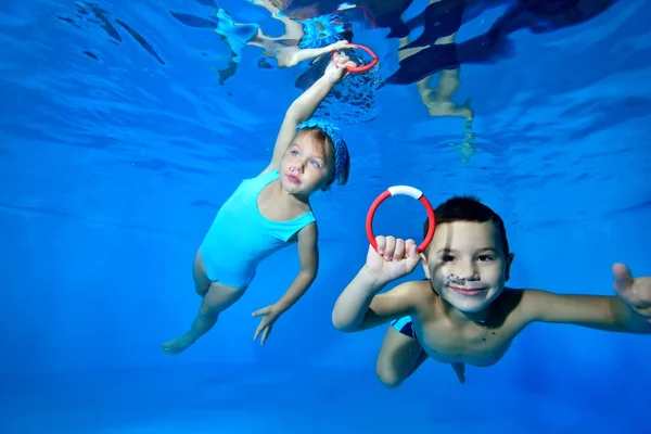 Niños felices, un niño y una niña, jueguen y diviértanse bajo el agua en la piscina infantil. Nadan con los ojos abiertos y recogen juguetes del fondo. De cerca. Concepto. Vista horizontal . — Foto de Stock