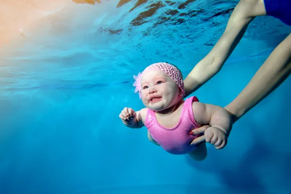 Primer plano de una niña sonriente nadando bajo el agua en una piscina infantil, con su madre apoyándola con sus brazos. Concepto. Foto digital. Orientación horizontal . — Foto de Stock