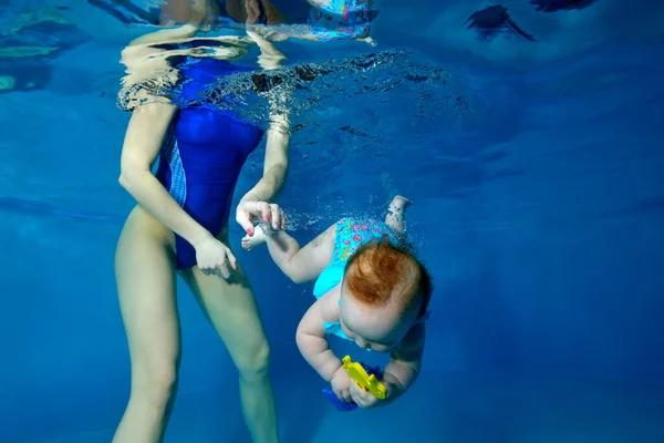 Una niña encantadora está nadando en una piscina para niños. Se zambulle bajo el agua con un juguete en las manos. Primer plano. Foto digital. Orientación horizontal . — Foto de Stock