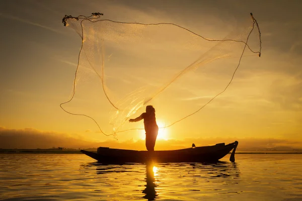 Silhueta de pescador asiático em barco de madeira, pescador em ação jogando uma rede para a captura de peixes de água doce no rio natureza, pescadores tradicionais ao pôr do sol na Tailândia — Fotografia de Stock