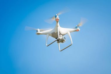 Beyaz dron açık mavi gökyüzünde süzülüyor