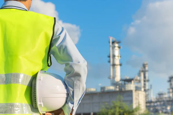 Інженерний чоловік стоїть з білим шоломом безпеки біля нафтопереробного заводу — стокове фото