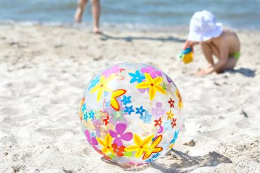 Çok renkli bir şişme top kum plaj üzerinde yer almaktadır. Çocuğun yanında şişme top çalışır. Yaz eğlence kavramı.