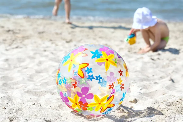 Çok renkli bir şişme top kum plaj üzerinde yer almaktadır. Çocuğun yanında şişme top çalışır. Yaz eğlence kavramı.
